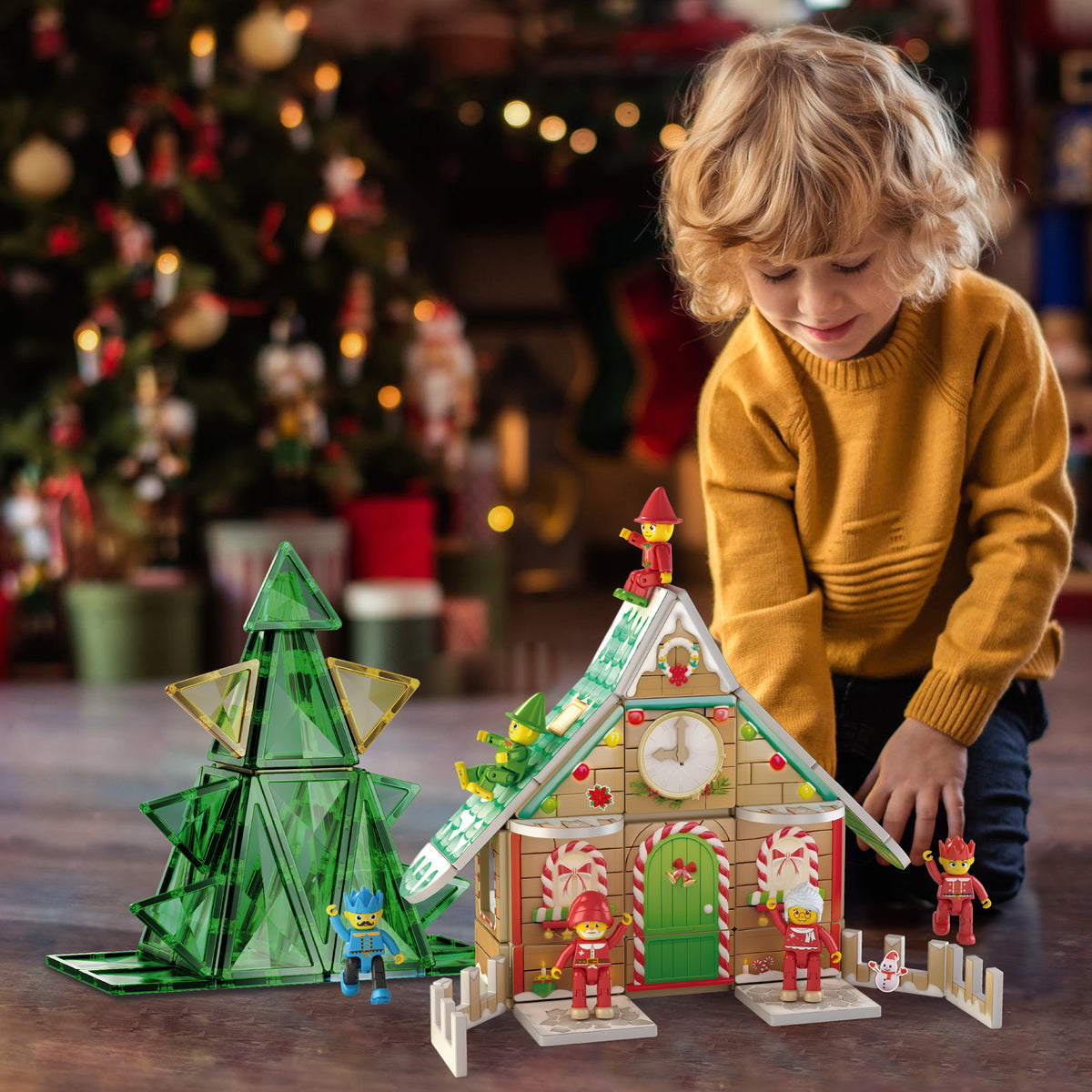 Young child playing on the floor with a Christmas-themed magnetic tile house, tree, and figures.   