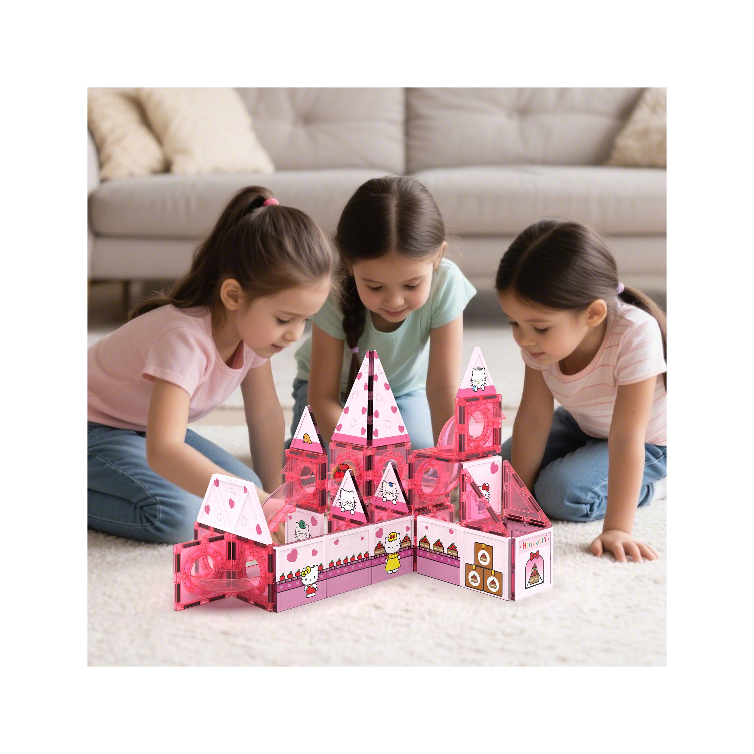 Three girls playing with a pink Hello Kitty magnetic tile castle toy on a carpet.