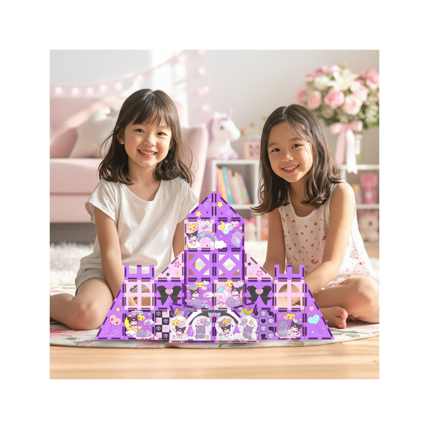 Two girls smiling next to a large purple Kuromi magnetic tile castle built on a rug in a playroom.