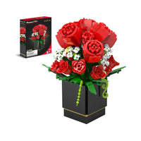 A bouquet of red roses and small white flowers made of toy building bricks in a black square vase, with product packaging.
