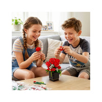Two happy children assembling a colorful building-block flower bouquet in a vase on a coffee table.