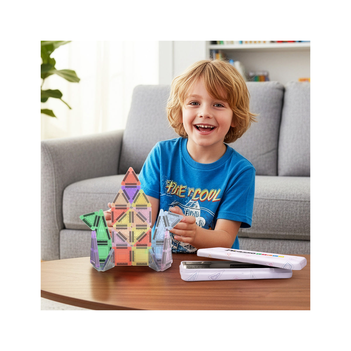 Smiling boy sitting by a table playing with a mini magnetic tile rocket next to its metal travel case.   
