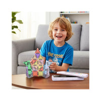 Smiling boy sitting by a table playing with a mini magnetic tile rocket next to its metal travel case.   