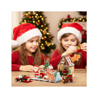 Two young girls wearing Santa hats playing with a Christmas-themed magnetic building set on a wooden table.
