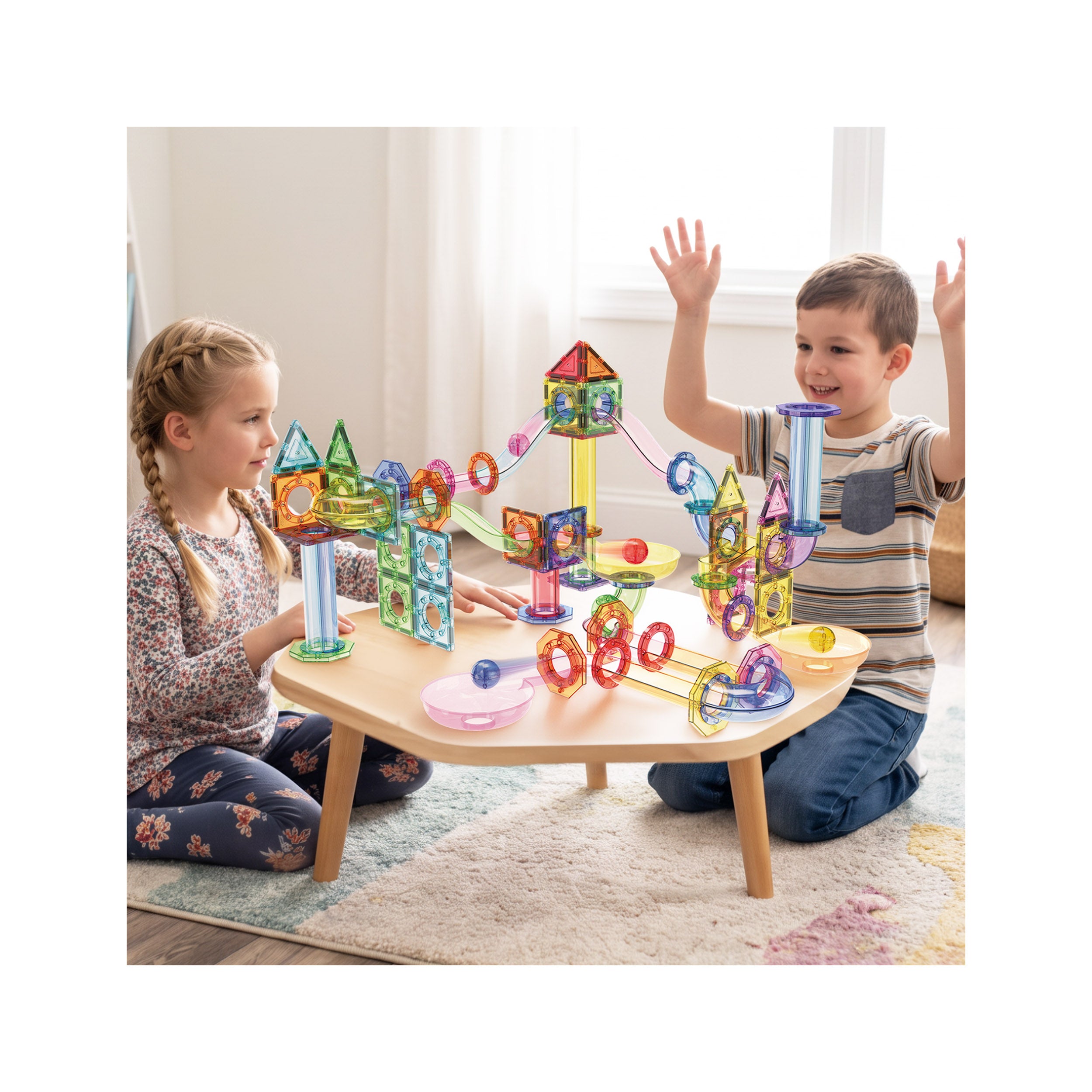 Two children playing with an assembled PicassoTiles magnetic marble run playset on a wooden activity table.