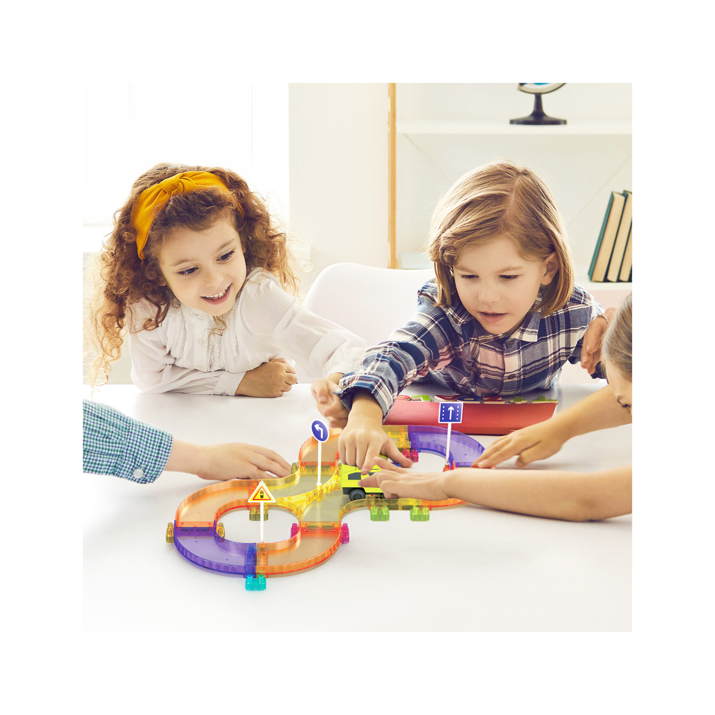 Children gathered around a table playing with a colorful figure-eight magnetic race track set and toy car.