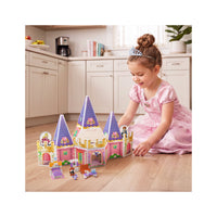 Young girl in princess dress playing with a pink magnetic tile castle and miniature toy furniture set.
