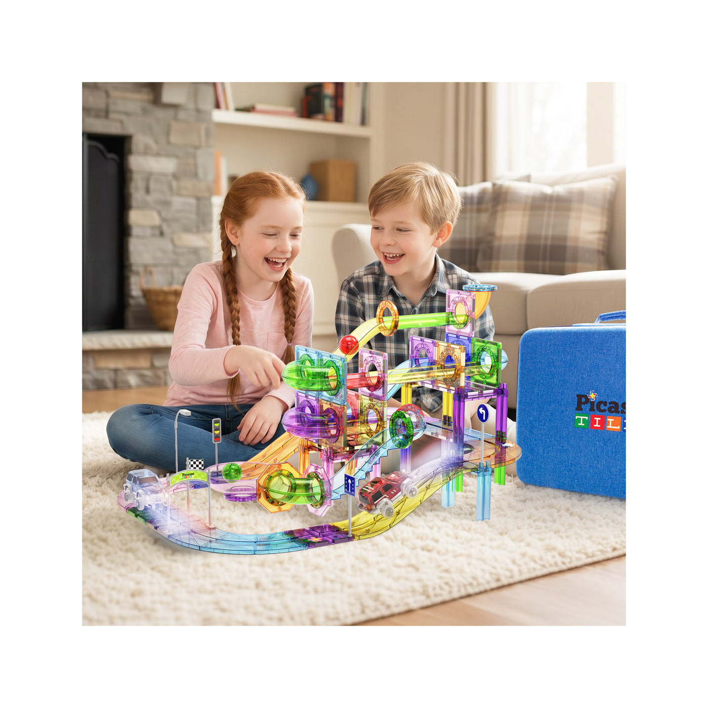 Two children sitting on a rug in a living room, playing with a colorful PicassoTiles magnetic marble run set.