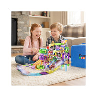 Two children sitting on a rug in a living room, playing with a colorful PicassoTiles magnetic marble run set.