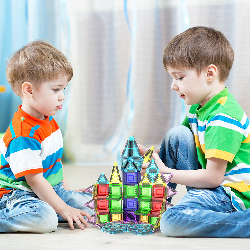 Two young boys sitting on the floor building a colorful magnetic tile castle together.   
